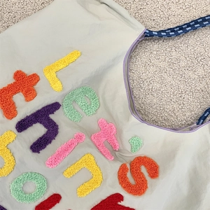 Detailed close-up of colorful chenille embroidery on a grey canvas tote bag