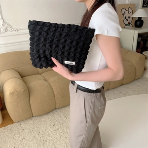 Detail of a black quilted bubble texture makeup bag held by a model in a soft home setting