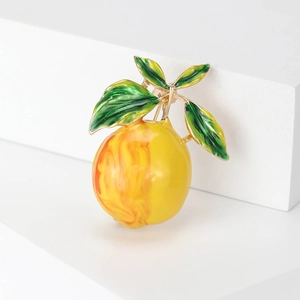 Fashionable lemon brooch with yellow enamel fruit and green leaves on white background
