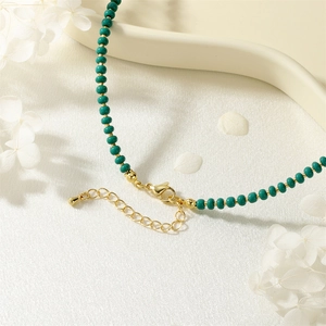 Macro detail of emerald beads and gold lobster clasp with extender chain on white silk