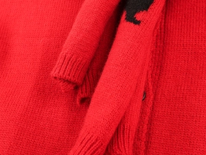 Macro detail of red knit cardigan texture featuring black button and ribbed cuff finish