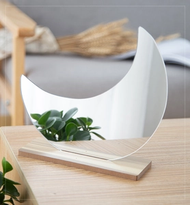 Irregular crescent acrylic mirror featuring a natural wood base on a cozy desktop setup