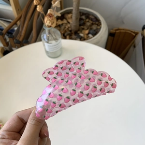 Detailed view of pink translucent strawberry print claw clip held against a desk