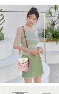 Detail of pink quilted crossbody bag with golden heart lock and woven strap worn by model