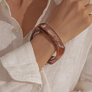 Detail of amber tortoiseshell resin thick bangle worn with a white linen shirt