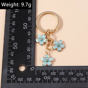 Detail of blue cherry blossom keychain with gold ring, weighing 9.7g on a pink backdrop
