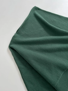 Detailed close-up showing the smooth texture and fine knit of the dark green sweater fabric