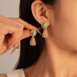 Detail of vintage geometric earrings with turquoise stones and textured gold pendants