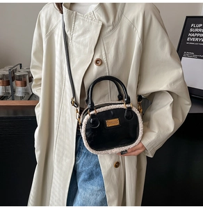Detail of black crossbody bag with white plush trim and golden logo plate on beige coat