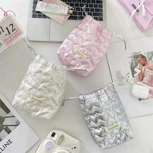 Macro detail of heart-quilted drawstring pouches in pink, white, and silver metallic PU