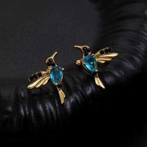 Detail of hummingbird ear cuff with blue zircon and gold plating on black texture