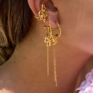 Detailed close-up of golden bow earrings and long tassel chain on model's ear