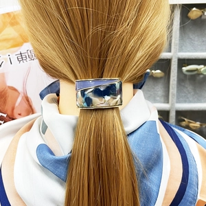 Detail of blue marble resin ponytail cuff with golden metal trim on model