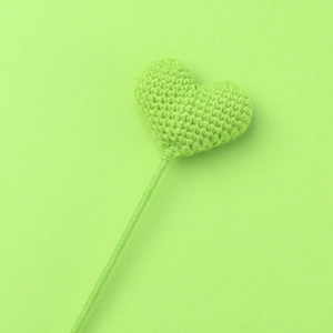 Detailed close-up of a lime green handmade crocheted heart flower on a slender stem