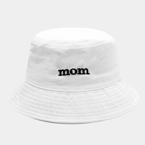 Dettaglio del ricamo nero 'mom' su un cappello a secchiello in cotone bianco