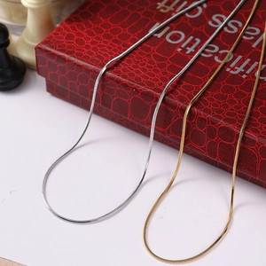 Close-up of gold and silver snake chain necklaces with a red gift box on a white surface