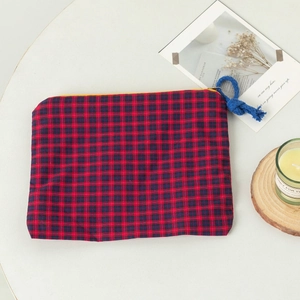 Detail der rot-blau karierten Baumwolltasche mit gelbem Reißverschluss auf weißem Tisch