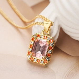 Macro shot of rectangular pink gemstone pendant with orange and white halo in gold finish