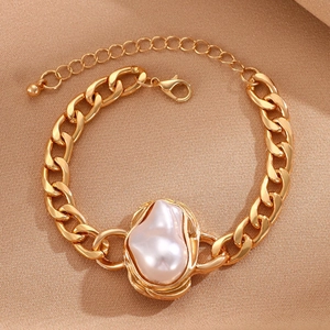 Detail of a chunky gold Cuban chain bracelet featuring a unique Baroque pearl and lobster clasp