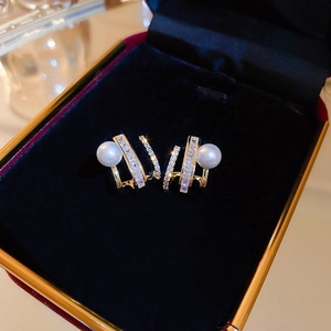 Macro detail of gold geometric claw earrings with white pearl and sparkling zircon stones
