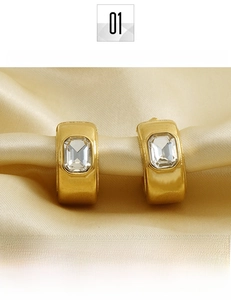 Détail de boucles d'oreilles C en acier titane doré 18K avec zircons taille émeraude