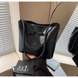 Detail of black glossy bucket bag featuring a decorative bow and slim shoulder strap
