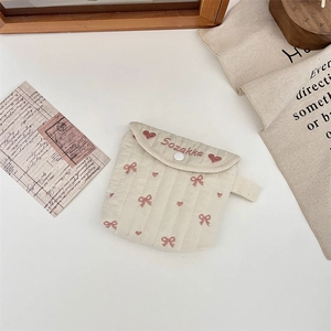 Dettaglio della borsa trapuntata crema con ricamo a cuore rosa e fiocco decorativo