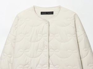 Detailed view of cream quilted jacket featuring unique bow patterns and snap-button collar
