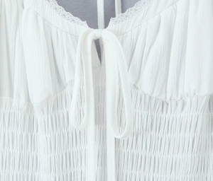 Close-up of white smocked dress detail with lace trim and elegant front tie design