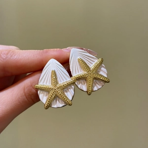 Nahaufnahme eleganter Seestern- und Muschelohrringe in Gold- und Weißoptik für den Urlaub.