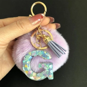 Détail d'un porte-clés pompon violet avec lettre G en résine et paillettes en cœur