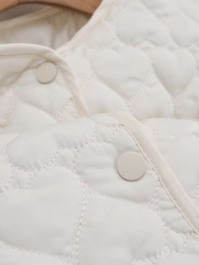 Close-up of cream quilted jacket featuring unique heart pattern stitching and matte buttons