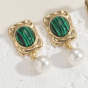 Macro detail of emerald green stone and white pearl earrings with gold metallic base