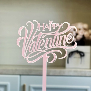 Macro shot of a pink acrylic Happy Valentine cake topper with a glossy artistic font