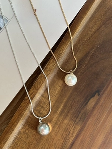 Detail of high-luster pearl pendants on gold and silver snake chains on a wooden tray