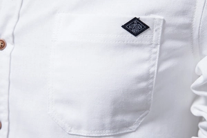 Close-up of white cotton shirt chest pocket with a black diamond logo label