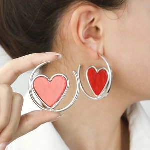 Chic silver hoop earrings with a bold red heart pendant on a female model
