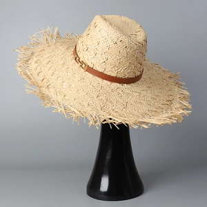Detail of wide-brim raffia hat featuring raw edges and brown leather strap with gold buckle