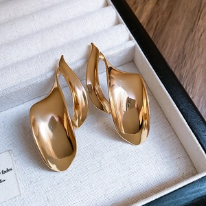 Macro shot of irregular golden metal stud earrings on a grey velvet jewelry tray