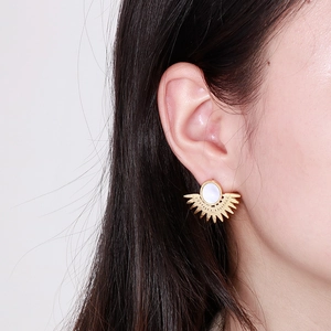 Détail de boucles d'oreilles soleil dorées avec incrustation blanche sur l'oreille