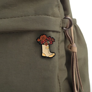 Détail d'une broche botte de pluie fleurie en émail épinglée sur un sac en nylon vert