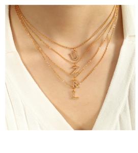 Close-up of layered gold titanium necklace with crystal-studded 'U Z R L' letter charms