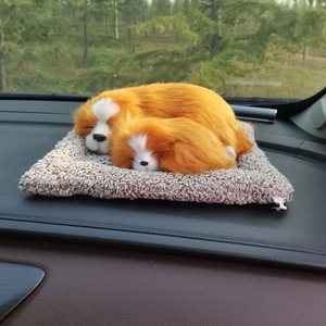 Realistic orange and white plush toy dogs sleeping on a beige mat on car dashboard