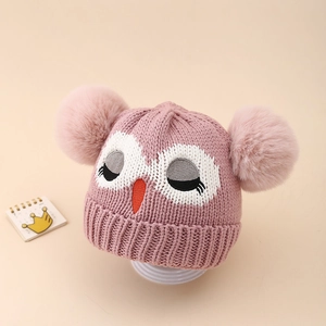 Détail d'un bonnet tricoté rose pour bébé avec broderie hibou et deux pompons