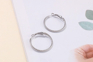 Detailed top view of large silver hoop earrings with woven texture on a white background