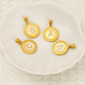 Gold stainless steel letter pendants A-D with white shell inlay in a decorative dish