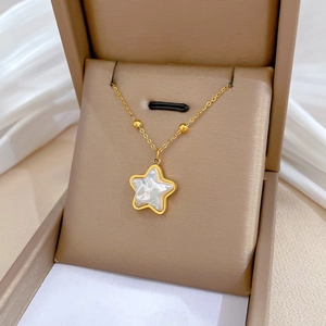 Gold star necklace with white shell inlay in beige jewelry box on white silk fabric