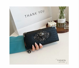 Detail of black faux crocodile leather clutch with silver skull ornament and corner protectors