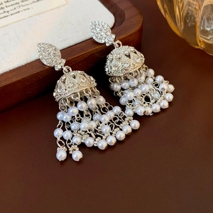 Macro view of crystal leaf and pearl tassel earrings on dark brown leather base