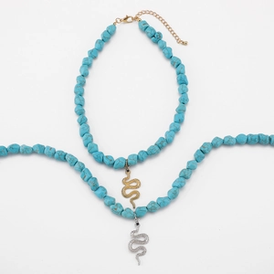 Detail of turquoise beaded necklace with gold and silver snake pendants on white surface